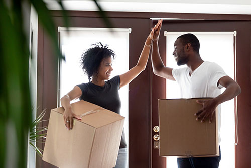 African American couple giving a high-five as they enter their new home with moving boxes.